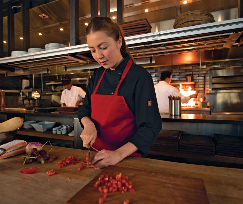 kitchen staff chopping tomatoes wearing a black chef coat and red apron